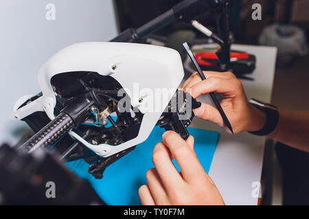 Closeup shot of man working on assembling new surveillance system using quadcopter drone with camera on table with different tools in modern workshop Stock Photo