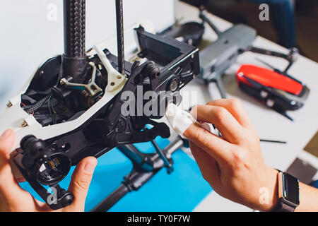 Closeup shot of man working on assembling new surveillance system using quadcopter drone with camera on table with different tools in modern workshop Stock Photo