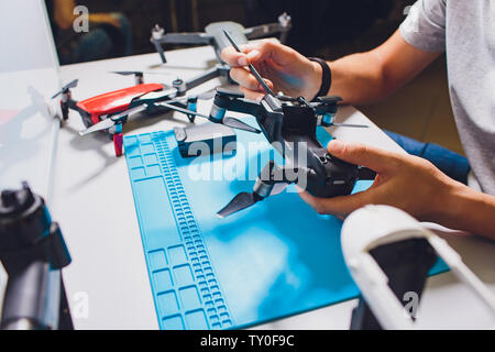 Closeup shot of man working on assembling new surveillance system using quadcopter drone with camera on table with different tools in modern workshop Stock Photo