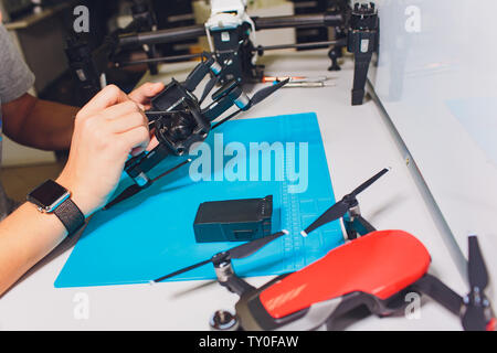 Closeup shot of man working on assembling new surveillance system using quadcopter drone with camera on table with different tools in modern workshop Stock Photo