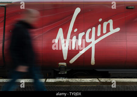 A man walks past the Virgin logo as seen on the side of one of the company's Pendolino trains. Stock Photo
