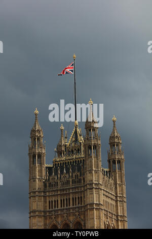 Top of tower with a flag pole and the union jack in the sunshine against a grey sky in London, in the afternoon in the month June.