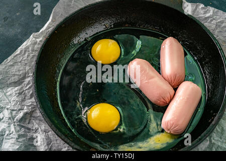 frying eggs with sausages in the pan with oil at the kitchen on the gas oven Stock Photo