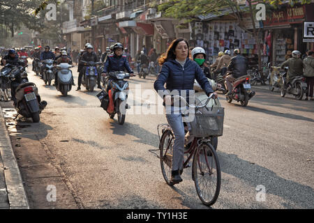 Hanoi, Vietnam - December 23, 2013: busy traffic of scooters and bikes on a street of Hanoi with a woman riding a bicycle in first plan Stock Photo