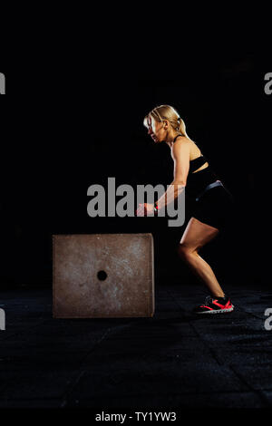 Shot of a young woman jumping onto a box as part of exercise routine