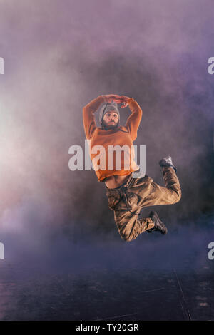 Male breakdancer jumps off high in the air while performing a cool dance move, a lot of smoke in the background. Stock Photo
