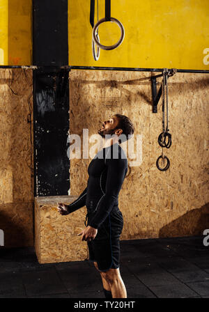 Fit young man in the black sportwear exercising with gymnastic rings in gym Stock Photo
