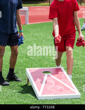 Two boys are playing a game of corn hole during a high school gym class on the turf. Stock Photo