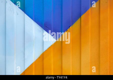 Background made of metal profile painted in blue, yellow and white on the fence or container backlit by the sun Stock Photo