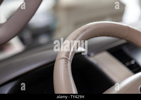 Car interior with a beige leather steering wheel close-up which is erased in the process of operation and needs restoration and repair in the workshop Stock Photo