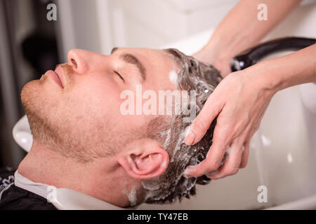 Master washes the head of the client in the Barber shop, hairdresser makes hairstyle for a young man. Stock Photo