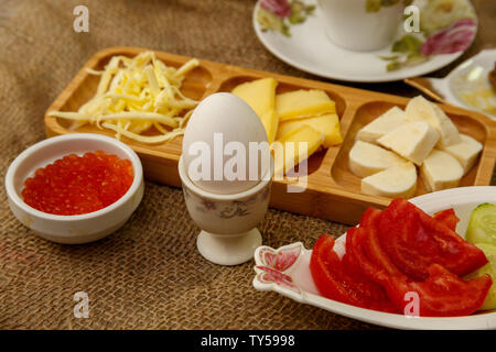 hearty and healthy Breakfast. tea in a Cup,different types of cheese on a wooden stand,sauces,boiled eggs,red caviar,cucumbers,tomatoes and jam. Stock Photo