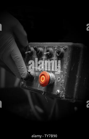 Man pressing button on an industrial machine control panel.  With lighting effect and selective colour Stock Photo
