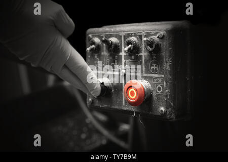 Man pressing button on an industrial machine control panel.  With lighting effect and selective colour Stock Photo