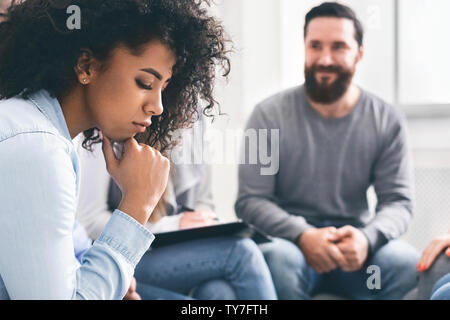 Depressed african woman sitting among cheerful people at therapy session Stock Photo