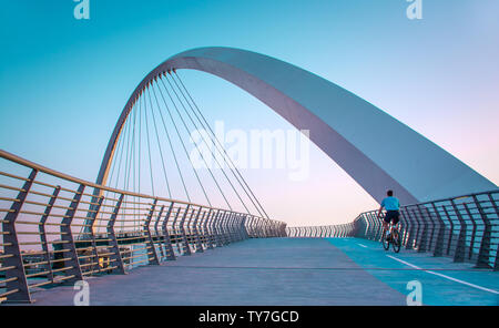 young man riding bicycle through Dubai water canal bridge famous attraction of Middle east modern architecture Bridge