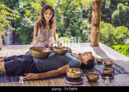 Nepal Buddha copper singing bowl at spa salon. Young beautiful man doing massage therapy singing bowls in the Spa against a waterfall. Sound therapy Stock Photo