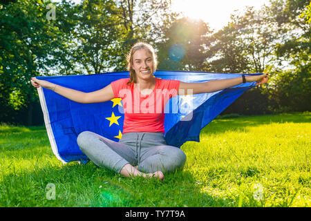 young woman is wearing a European flag behind and smiles Stock Photo