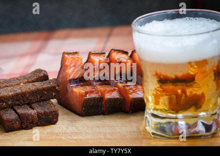 A glass of light beer with smoked fish and black fried bread in garlic. Beer and beer snack on a wooden Board close-up. Stock Photo