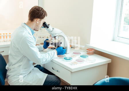 Handsome nice man sitting in front of the microscope Stock Photo