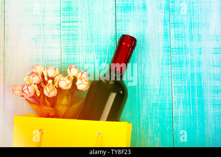 a bottle of wine in a yellow package as a gift, next flowers, gifts, copy space, on blue wooden background, to give girls a set of gentlemen for Datin Stock Photo