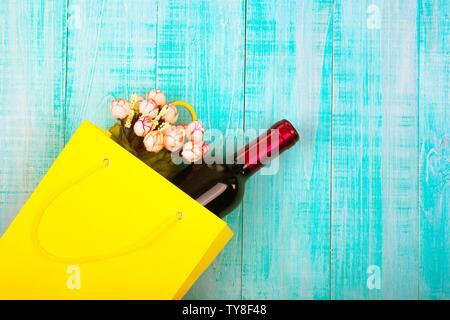 a bottle of wine in a yellow package as a gift, next flowers, gifts, copy space, on blue wooden background, to give girls a set of gentlemen for Datin Stock Photo