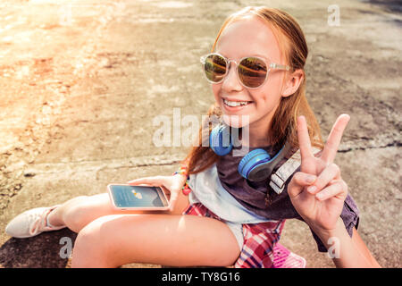 Pretty little girl with wide smile wearing dark sunglasses while showing her mood Stock Photo