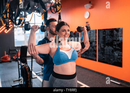 Obese woman doing exercises with barbells with help of trainer Stock Photo