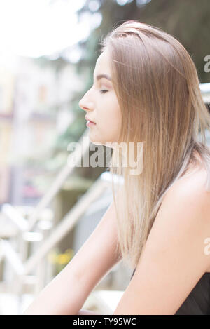 Attractive woman with blonde hair sitting on the stairs with closed eyes. Lifestyle photography. Blurred backgroud behind. Poland Stock Photo