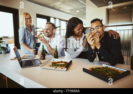 Diverse group of smiling office colleagues sitting at a table together after work having pizza and drinking beers Stock Photo