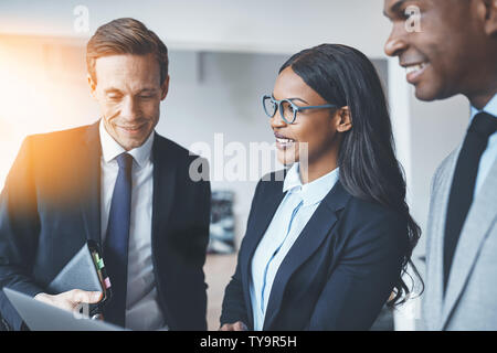 Smiling African American businesswoman discussing work on a laptop with colleagues while standing together in a bright modern office Stock Photo