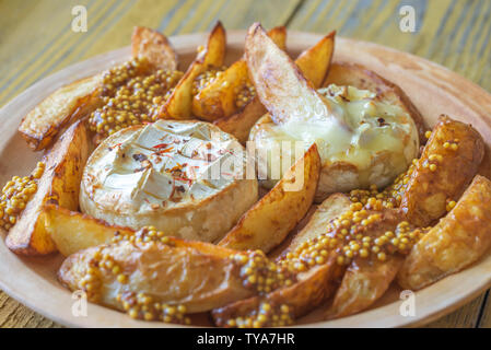 Baked Camembert cheese with roasted potatoes on the plate Stock Photo