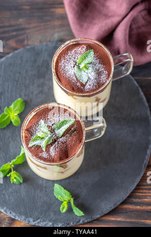 Two glass mugs of tiramisu decorated with cocoa and fresh mint leaves Stock Photo