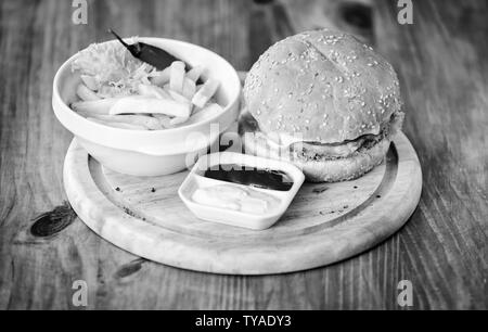 Burger menu. High calorie snack. Hamburger and french fries and tomato sauce on wooden board. Fast food concept. Burger with cheese meat and salad. Cheat meal. Delicious burger with sesame seeds. Stock Photo