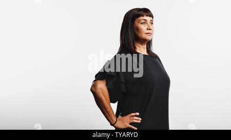 Side view of middle aged woman standing with her hand on waist. Woman standing against white background looking away. Stock Photo