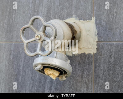 Close-up of gray fire hydrant on an outer wall of the building. There are no lid with a seal and someone put a stone into the nozzle for hose connecti Stock Photo