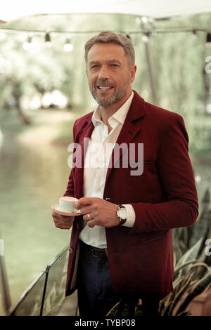Man smiling while drinking coffee standing near lake Stock Photo