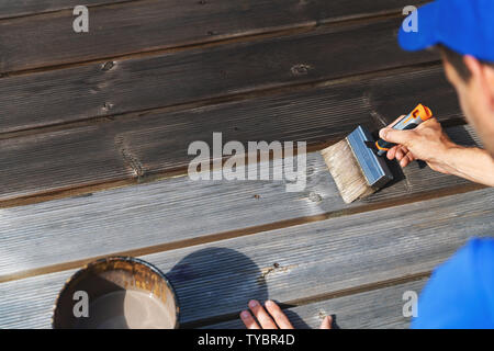 man restores wooden patio deck with wood protective paint Stock Photo