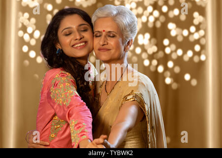 mother and daughter wearing traditional clothing, embracing while posing happily together interacting on diwali festival Stock Photo