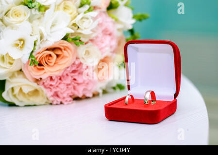 Gold wedding rings in a red box next to the bride's bouquet Stock Photo