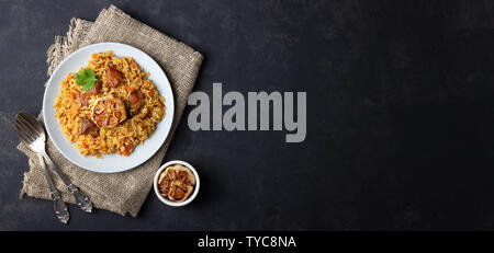 Traditional asian dish - pilaf from from rice, vegetables and meat in a plate on black background. Top view. Long format. Stock Photo