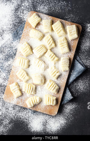 Raw uncooked homemade potato gnocchi with flour on cutting board. Top view. Dark background. Stock Photo