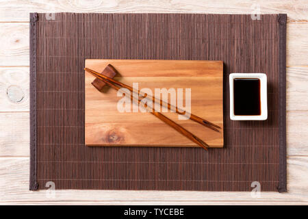Empty rectangular wooden plate for sushi with sauce and chopsticks on wooden table, top view. Stock Photo