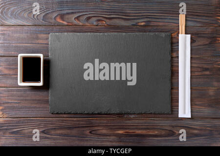 Empty rectangular black slate plate with chopsticks for sushi and soy sauce on wooden background. Top view with copy space. Stock Photo