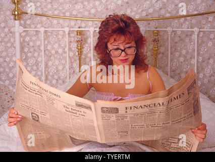 Historical archive young business woman wearing glasses returns to bed reading October 27th 1986 edition of the Financial Times before leaving for work archival1980s image of the way we were in 80s England UK Stock Photo