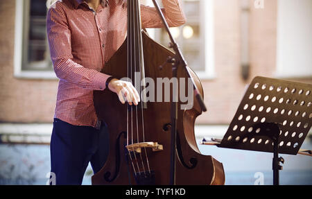 A professional musician, dressed in a pink plaid shirt and blue pants, plays a jazz melody on a string-bow instrument - contrabass without a bow Stock Photo