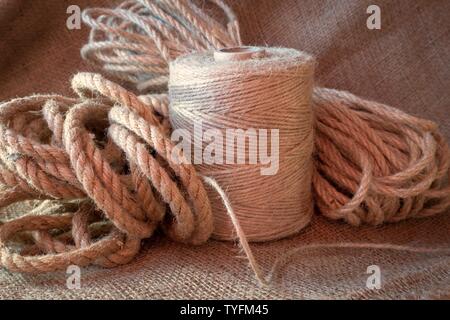 Jute rope and spools of burlap threads or jute twine on sackcloth fabric in close-up Stock Photo