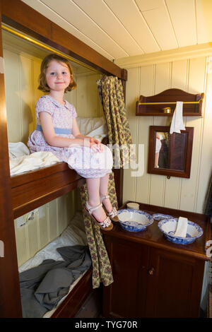 Young child girl / kid aged four, in a cabin room / cabin rooms / bedroom / bed room with bunk beds berth to illustrate first class passenger life on board the SS Great Britain. Promenade saloon deck. Brunel's ship is now a museum attraction in drydock at Bristol, UK England (109)