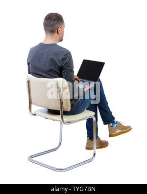 Back view of a man who sits on a chair with a laptop. Rear view people collection. Young guy in a gray jacket sitting working on a laptop. backside vi Stock Photo