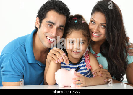Indian girl putting coin into a piggy bank with her parents Stock Photo